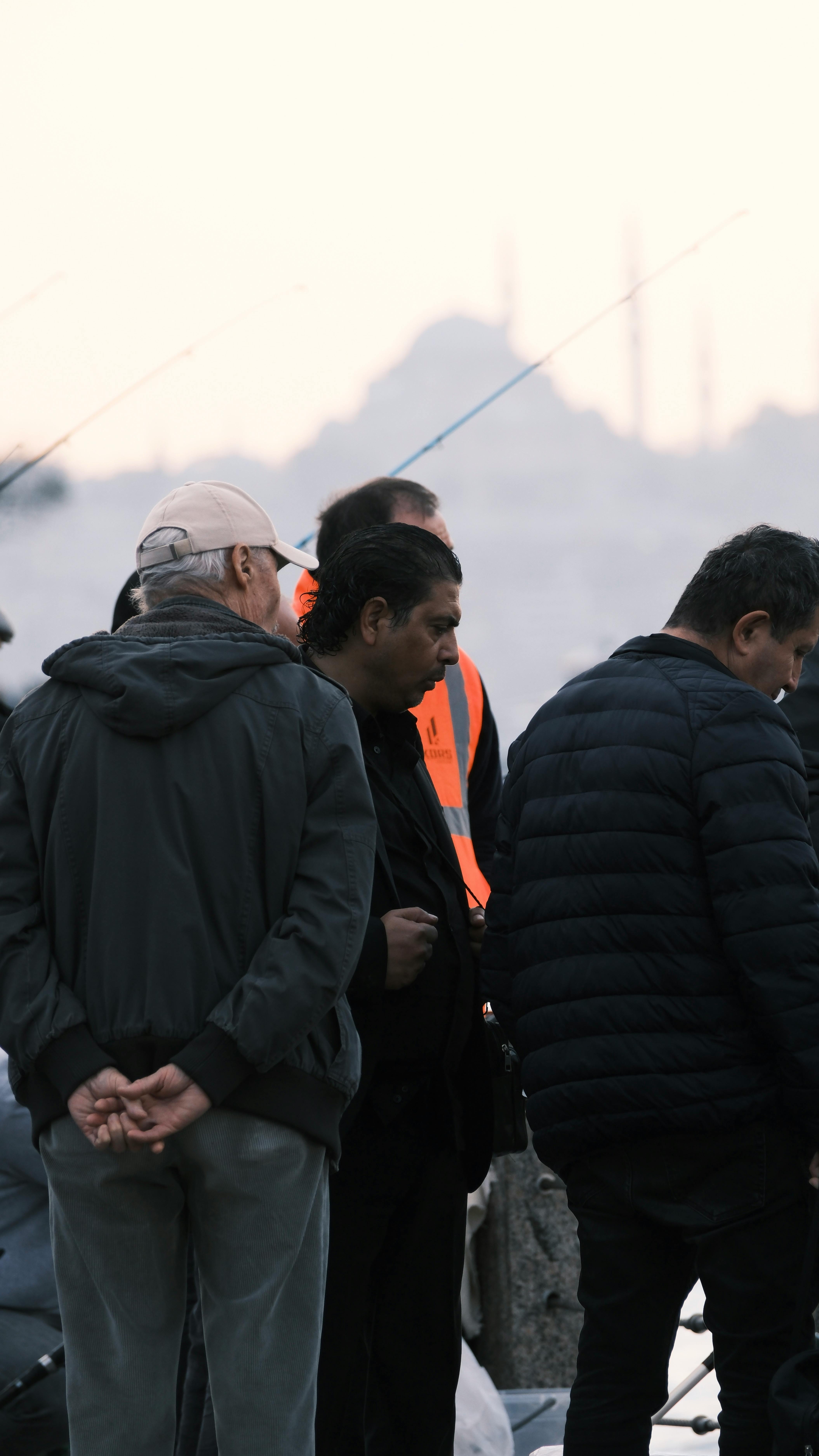 A group of adults fishing by the water at sunrise with cityscape background.