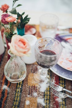 一张摆满鲜花和餐具的五彩桌子上，酒杯的特写营造出优雅的用餐氛围