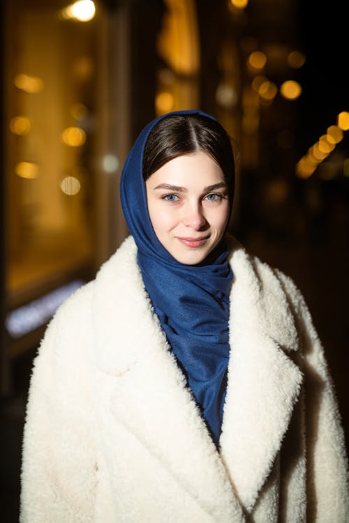 Young Woman Wearing a Coat and a Scarf Standing on the Background of Lights 