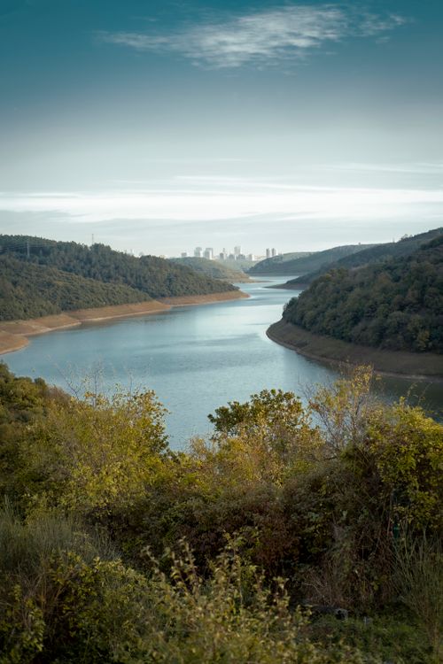 Free Peaceful river winding through lush forest with Istanbul skyline in the distance, under a clear sky. Stock Photo