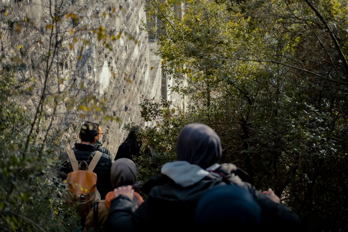 Free Group of hikers navigating a forested path beside a stone wall, embracing nature. Stock Photo