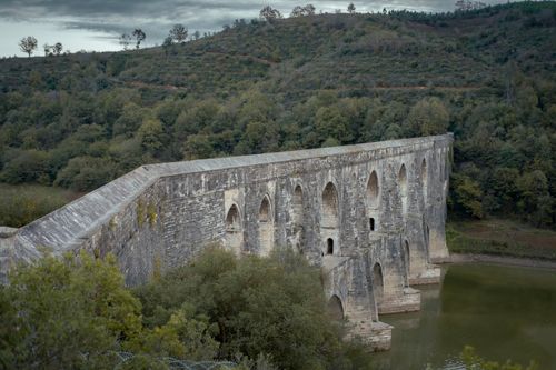 Free Historic stone bridge spanning a tranquil river amidst lush greenery. Stock Photo