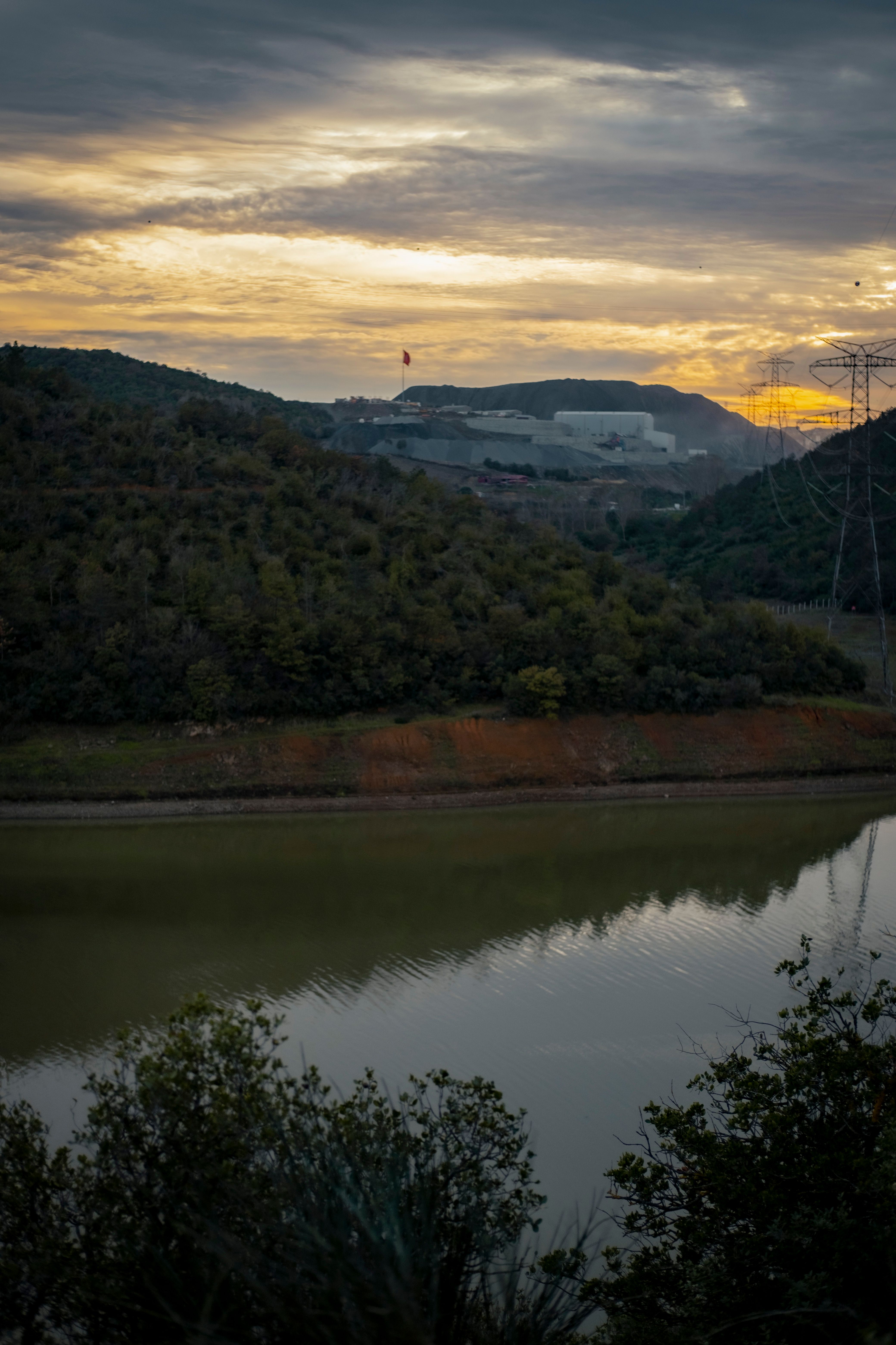 Calm river with hills reflecting at dusk under a dramatic sky.