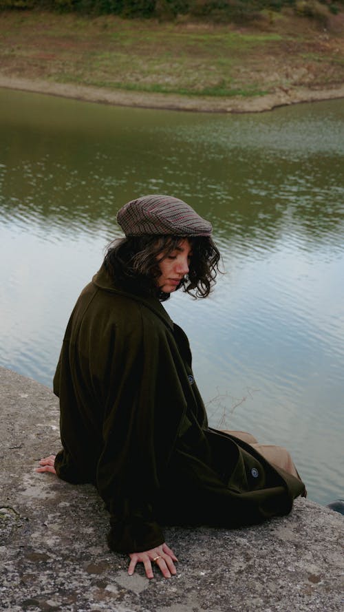 Woman in Check Flat Cap and Woolen Coat Sitting by River
