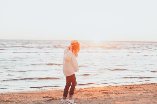 Free A woman walks on a sunlit beach, enjoying a peaceful summer day by the ocean. Stock Photo