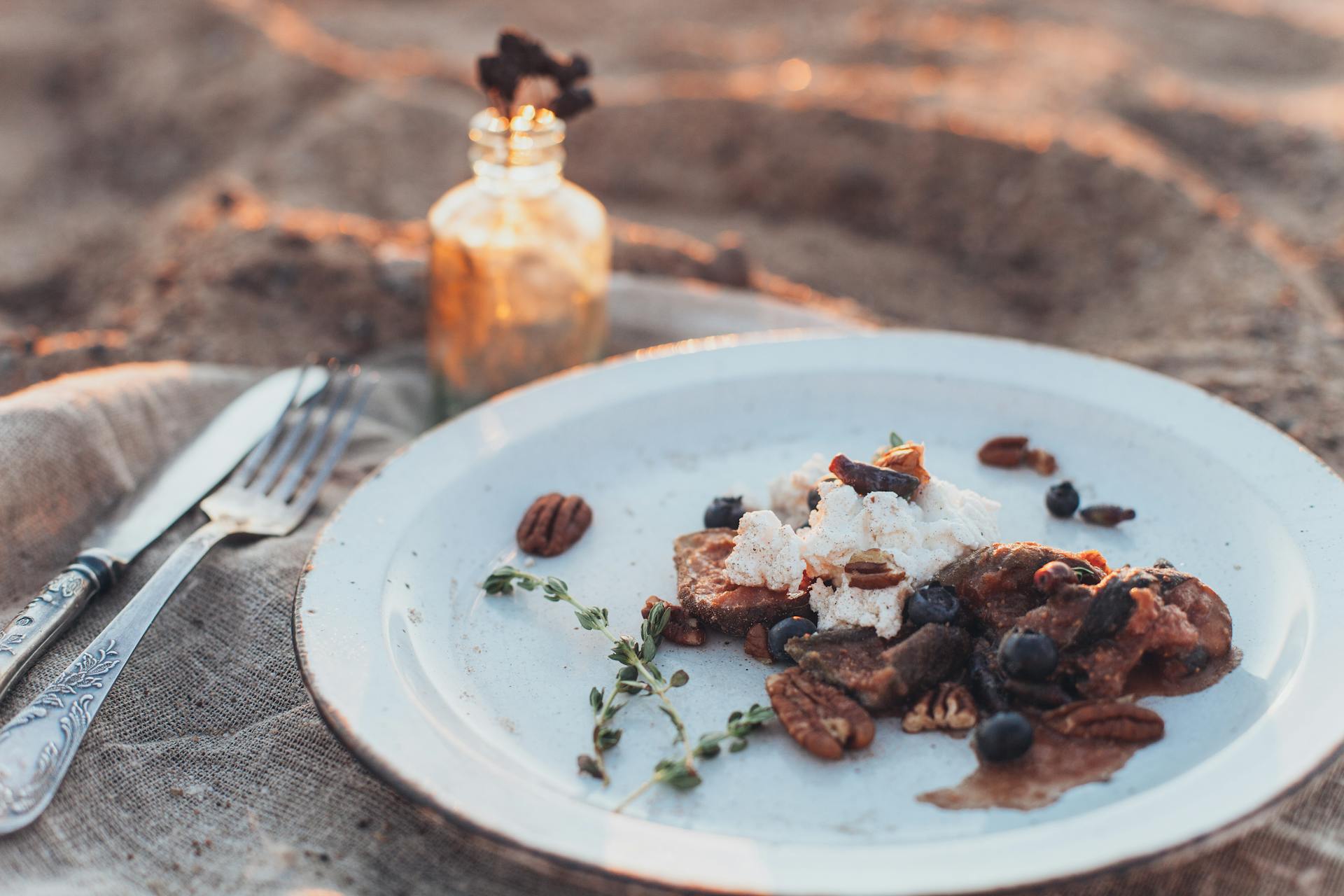 A rustic outdoor dining scene featuring a dessert plate with pecans and blueberries, lit by warm sunlight.
