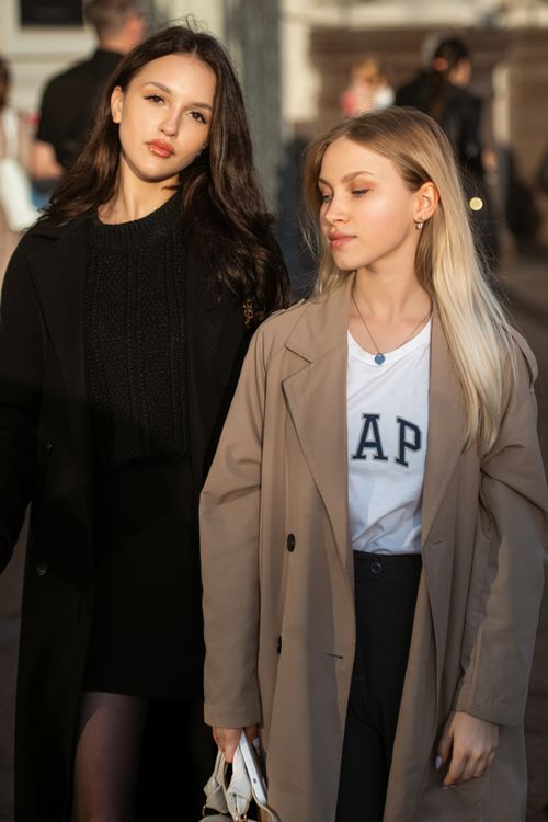 Free Two fashionable young women in elegant coats posing on a sunlit city street. Stock Photo
