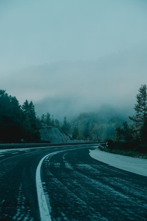 Free A winding road leads through a misty mountain landscape dusted with snow and shrouded in fog. Stock Photo