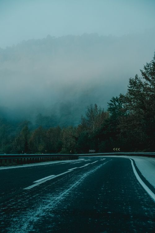 Free Misty road through mountains with fog and trees during winter, offering a serene and mysterious atmosphere. Stock Photo