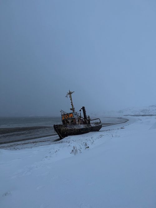 Free Rustic boat rests abandoned on a snow-covered beach in winter, surrounded by serene coastal fog. Stock Photo