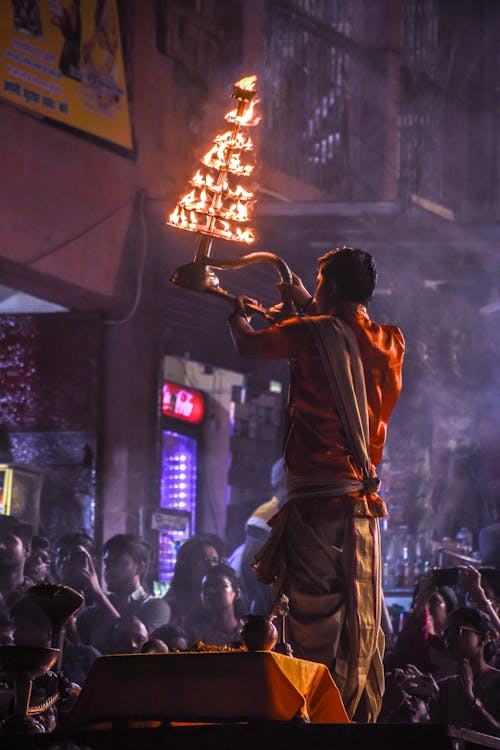 A Man in Traditional Clothing Holding Burning Candles in the Air during a Ceremony 