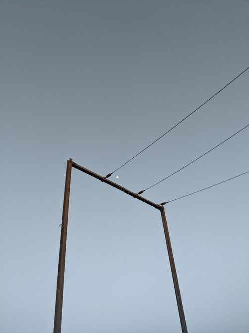 Free Minimalist photograph of power lines under a clear sky with visible moon, creating a serene atmosphere. Stock Photo