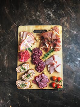 Delicious selection of cold cuts and bread on a wooden board with fresh herbs and tomatoes.