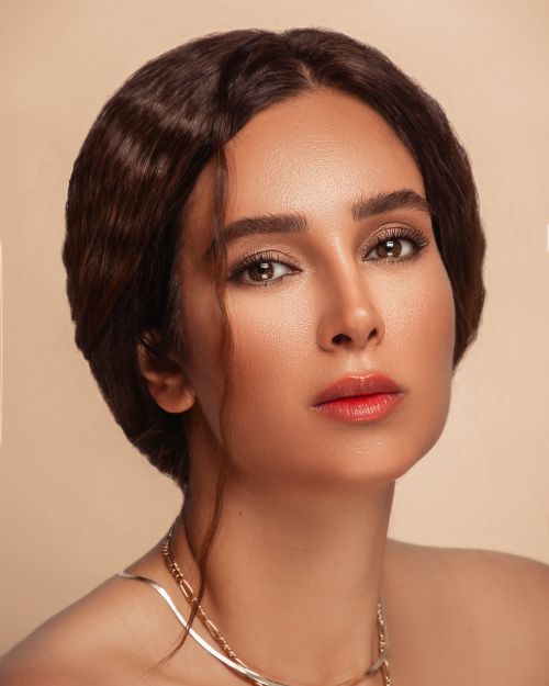 Free Close-up portrait of a brunette woman wearing a necklace against a beige background. Stock Photo