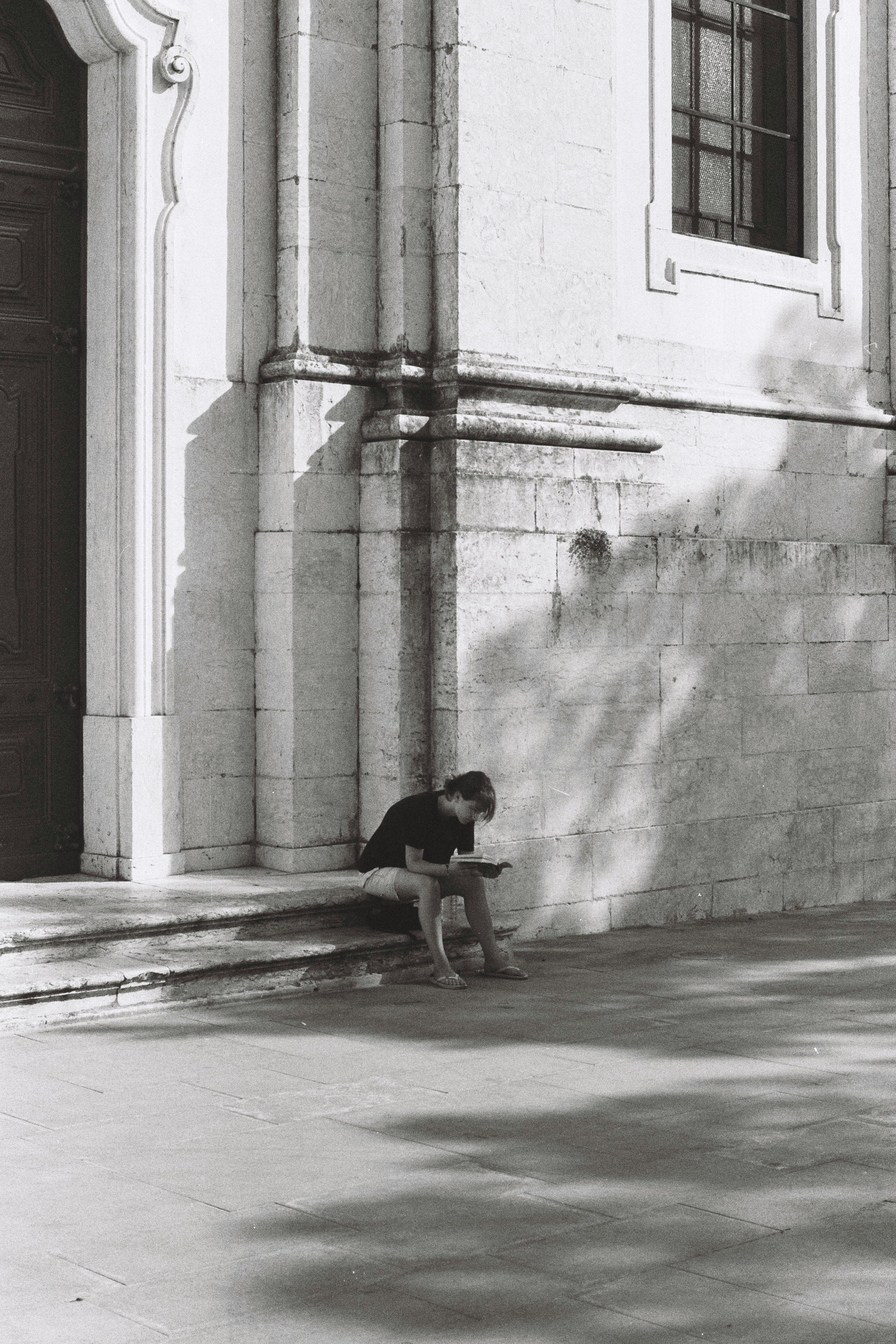Black and white photo capturing person sitting and reading on urban steps in Lisbon.