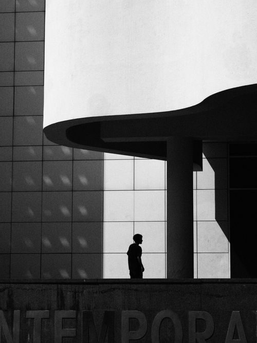 Free Silhouette of a person walking by a contemporary building in black and white. Stock Photo