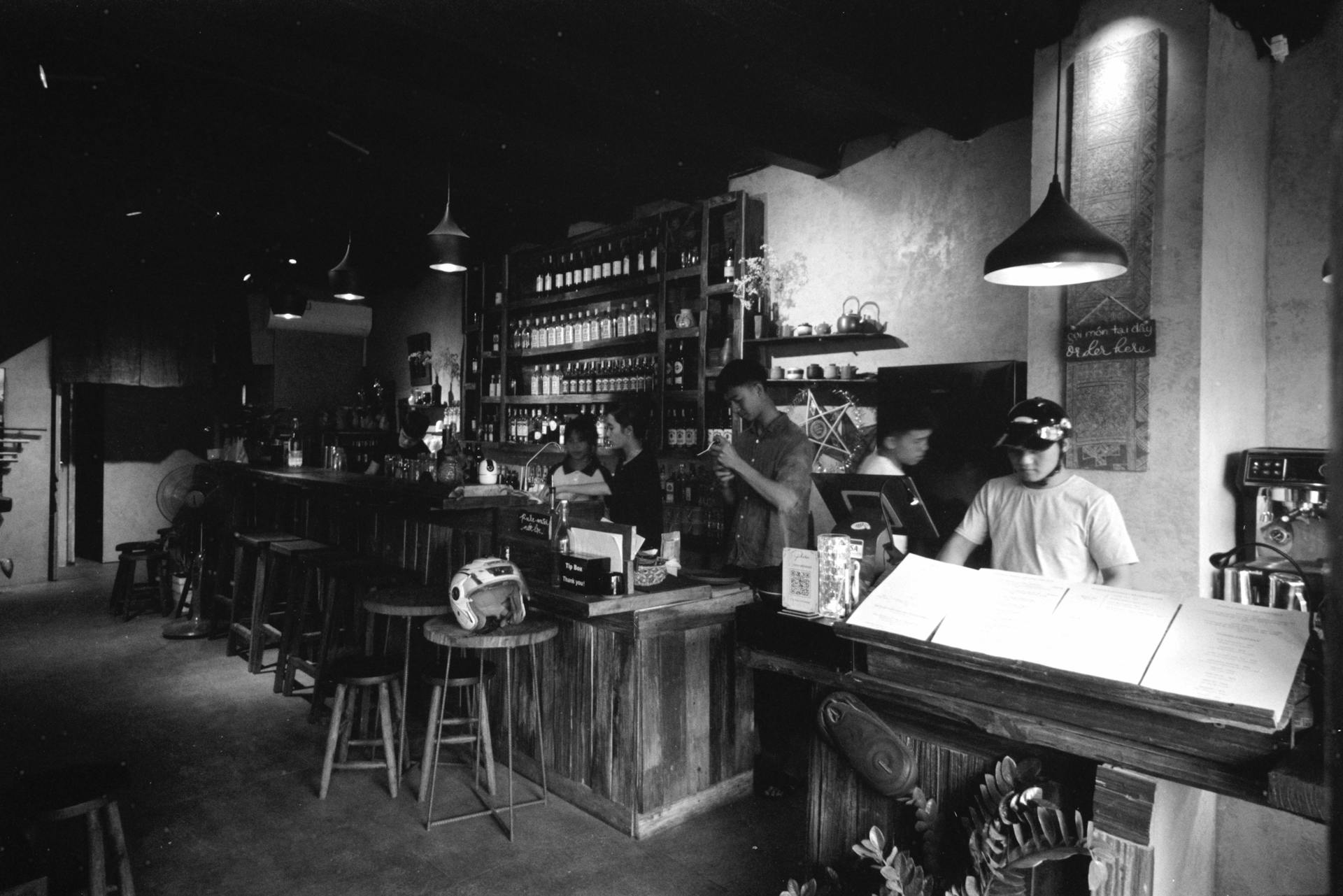 A cozy bar interior captured in black and white, featuring patrons and staff working behind the counter.