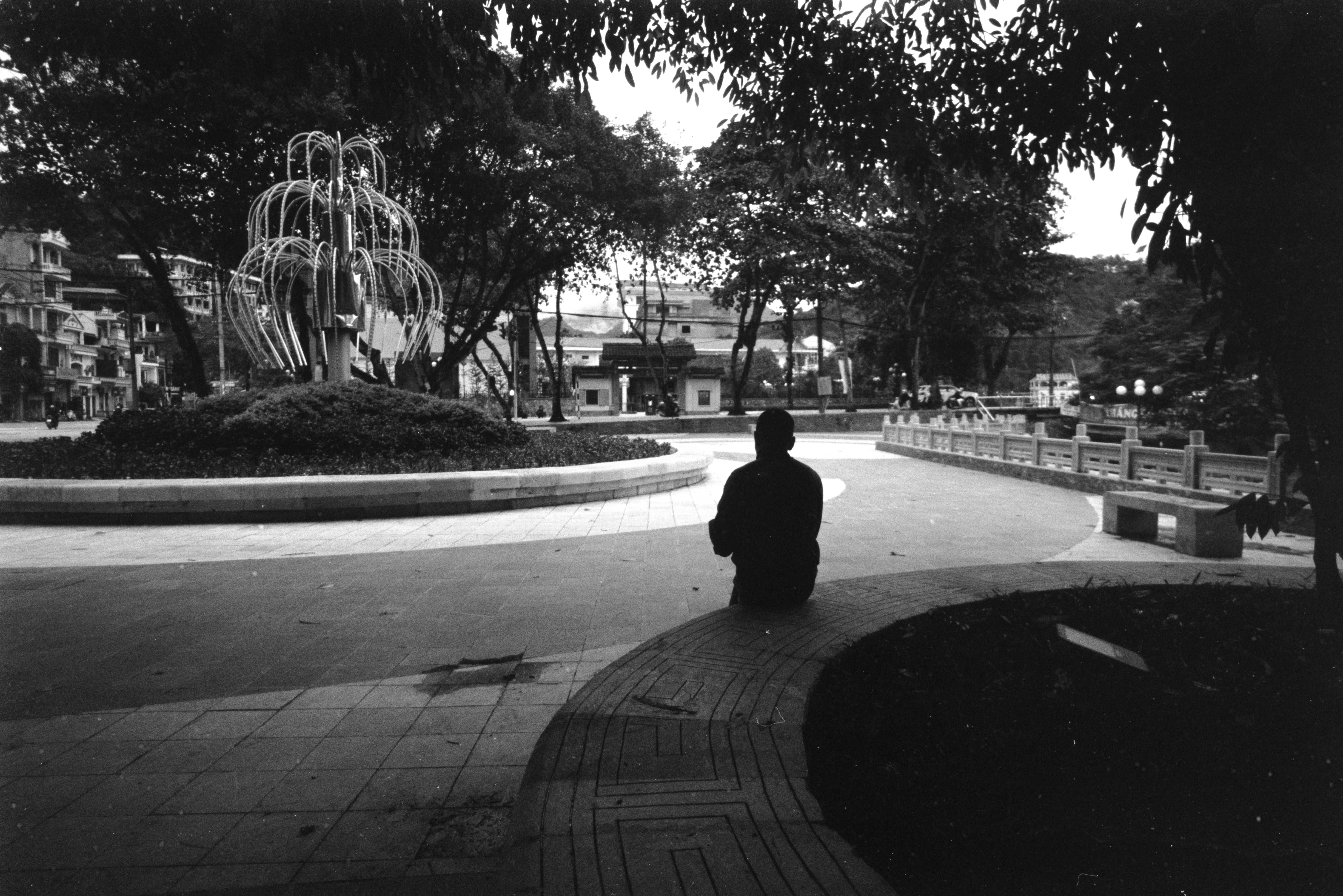 Silhouette of a person sitting peacefully in a city park with fountain.