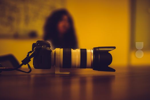 A Canon lens and camera on a wooden table indoors with a blurred person in the background.