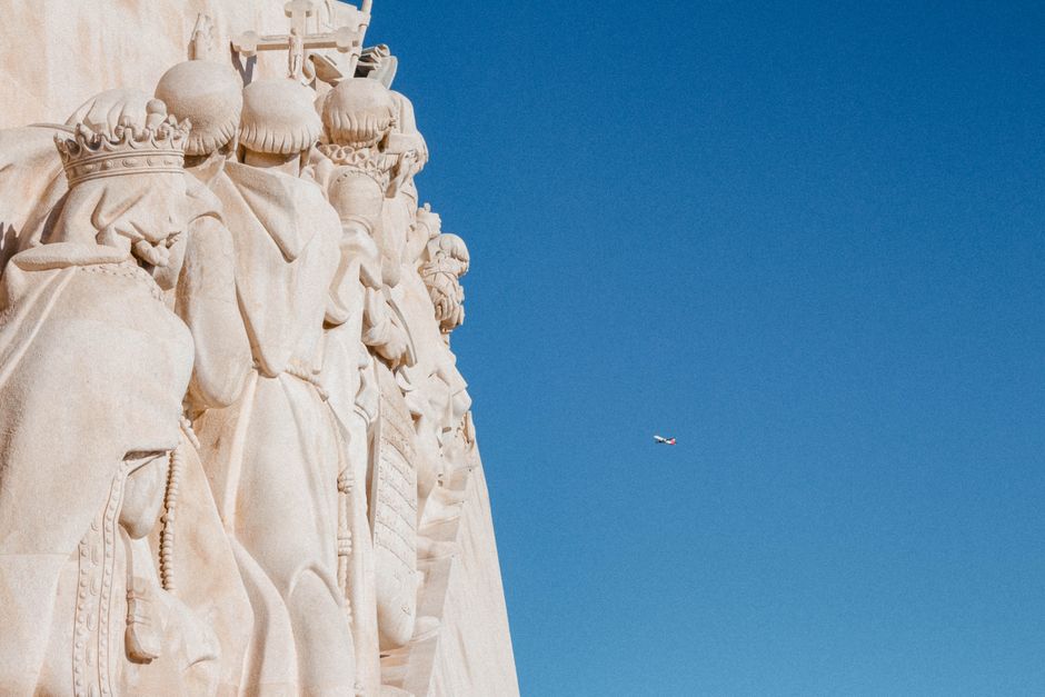 Low angle view of intricate sculptures against a clear sky with an airplane in the background in Lisbon, Portugal.