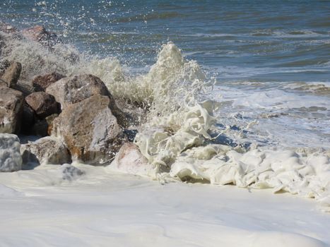 Dynamic wave action against rocks, creating foamy splashes along the beach.