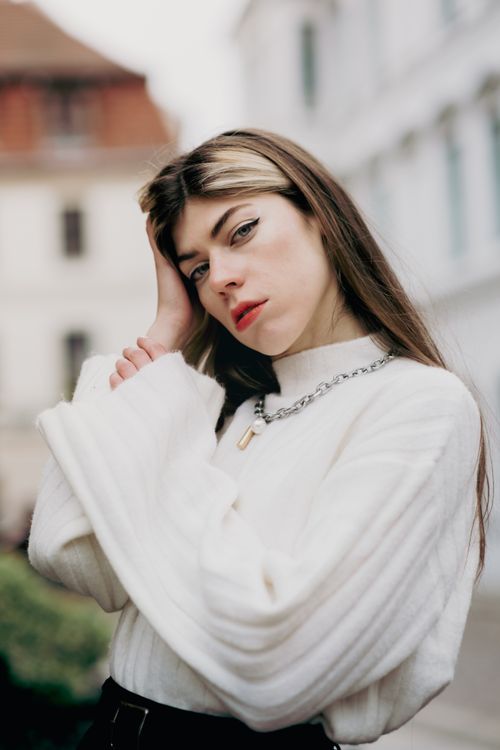 Free Stylish woman with long hair and makeup posing outdoors in white sweater and necklace. Stock Photo