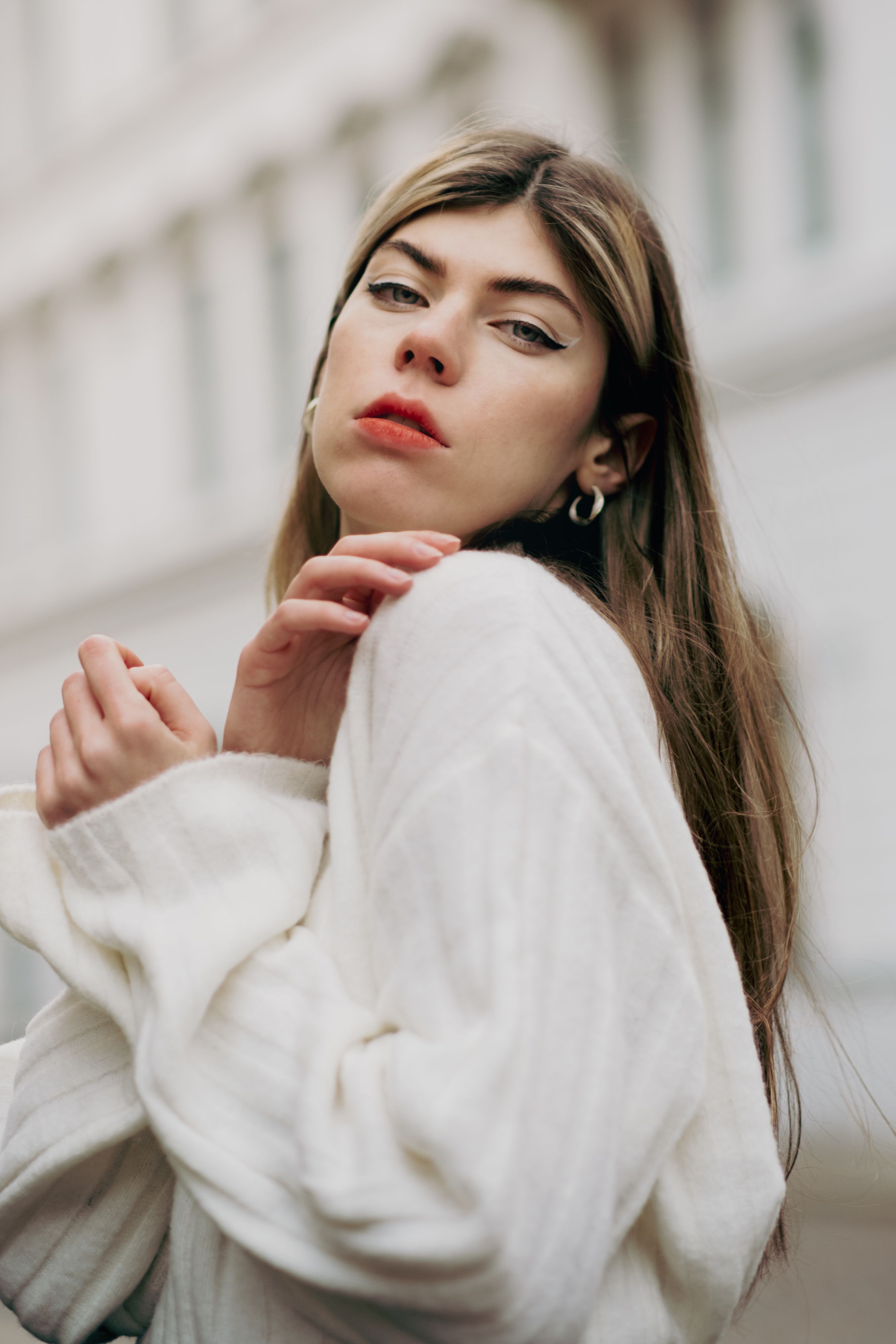 Portrait of a stylish young woman posing outdoors in a white sweater.