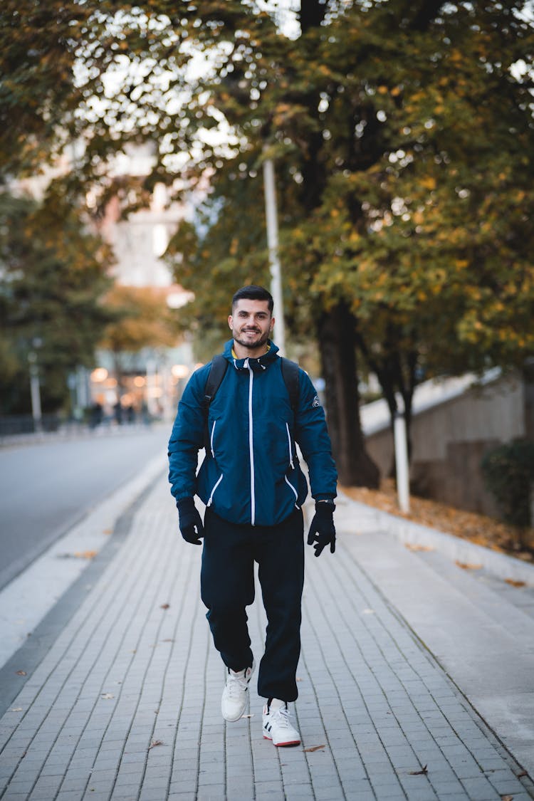 Young Man Walking On The Sidewalk In City And Smiling 