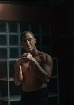 Portrait of a shirtless man with muscular build in dimly lit industrial setting.