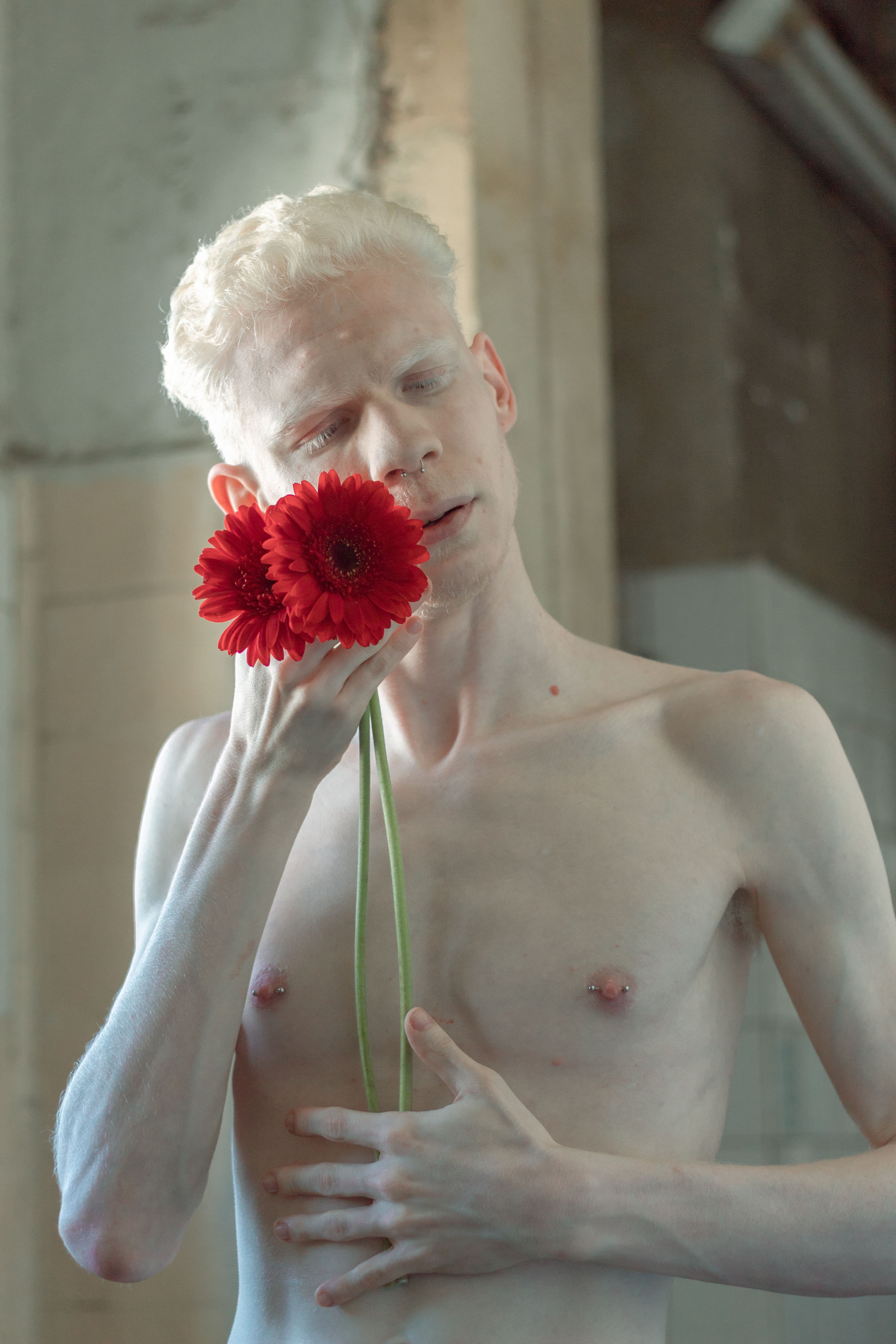 albino man posing shirtless and holding red flowers
