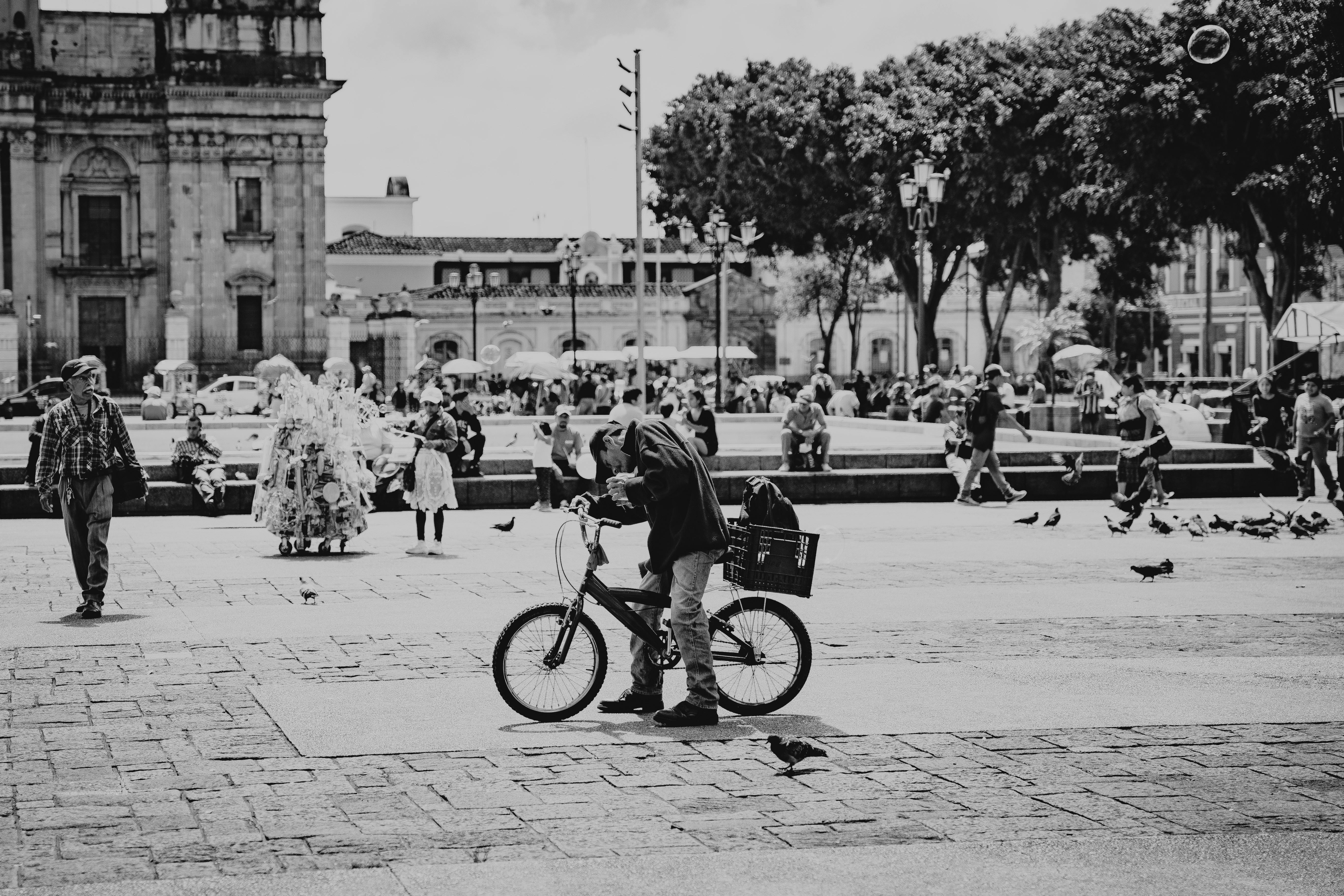 A bustling city square scene in black and white, featuring a cyclist among urban crowds.