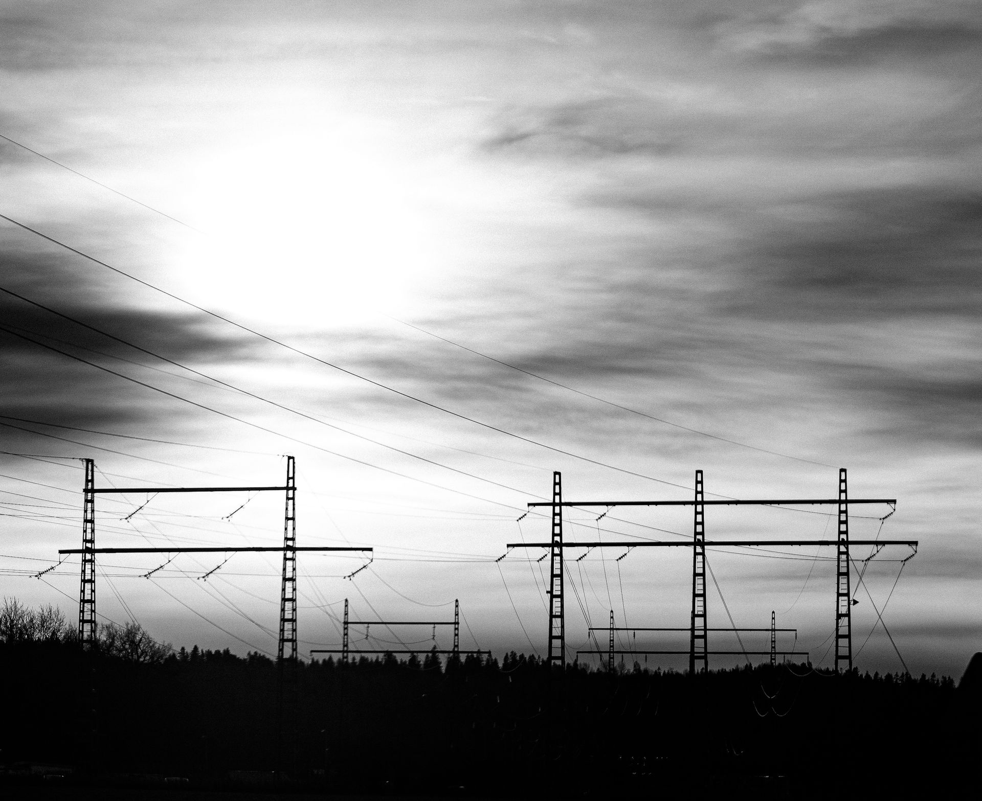 Dramatic black and white landscape of power lines against a cloudy sky, highlighting energy infrastructure.