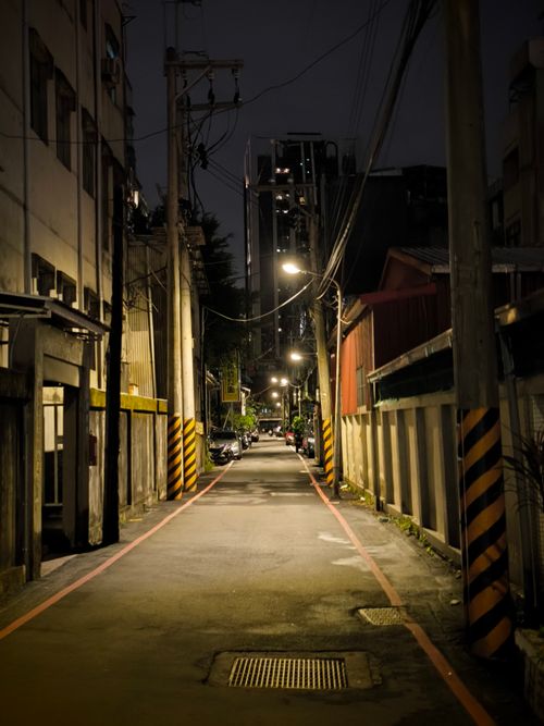 Free Dimly lit urban alleyway at night with streetlights and buildings lining the narrow street. Stock Photo