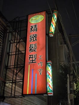 Brightly lit Chinese hair salon sign on an urban street at night, featuring colorful designs.