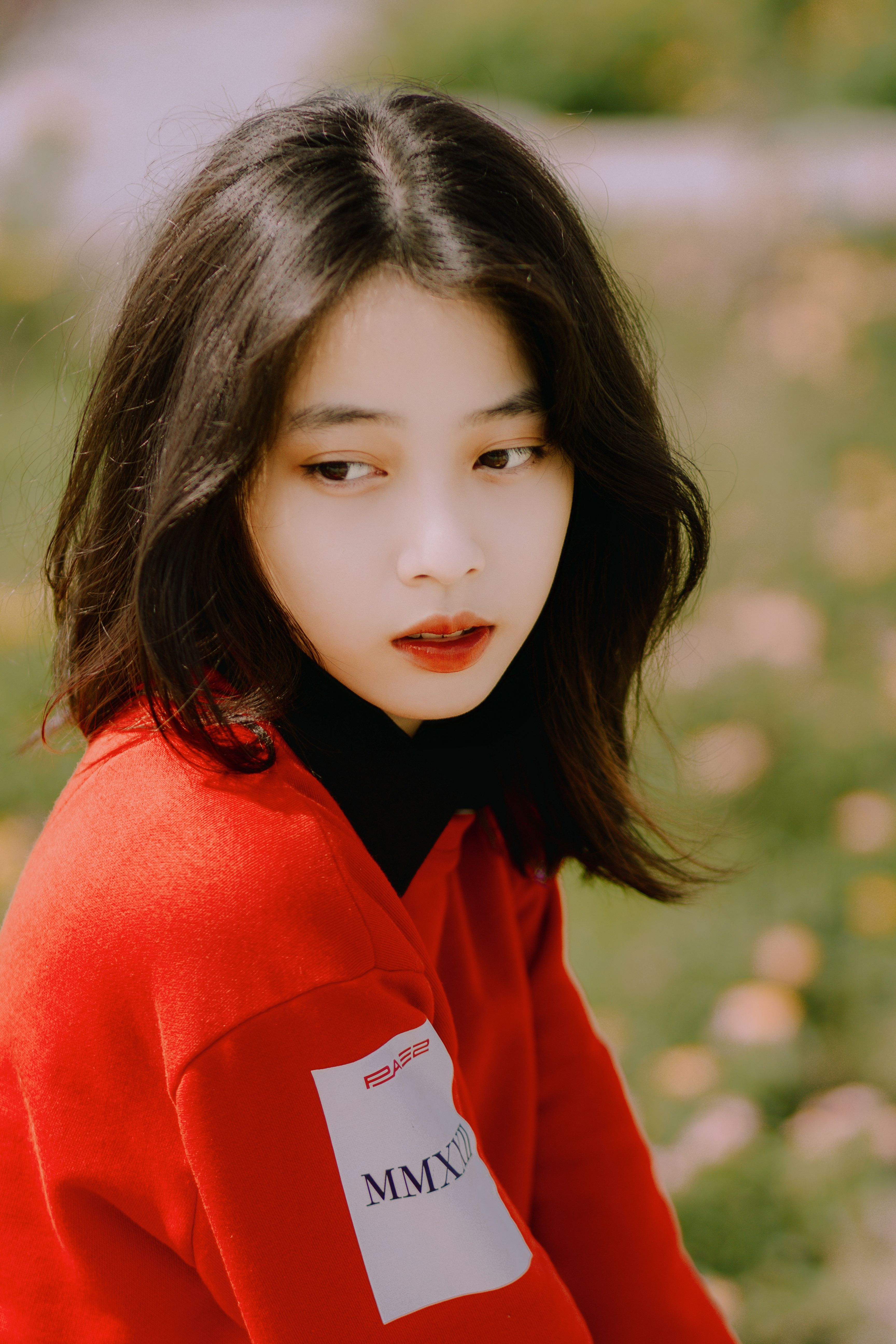 Portrait of a young woman in a red sweater sitting outdoors with a thoughtful expression.