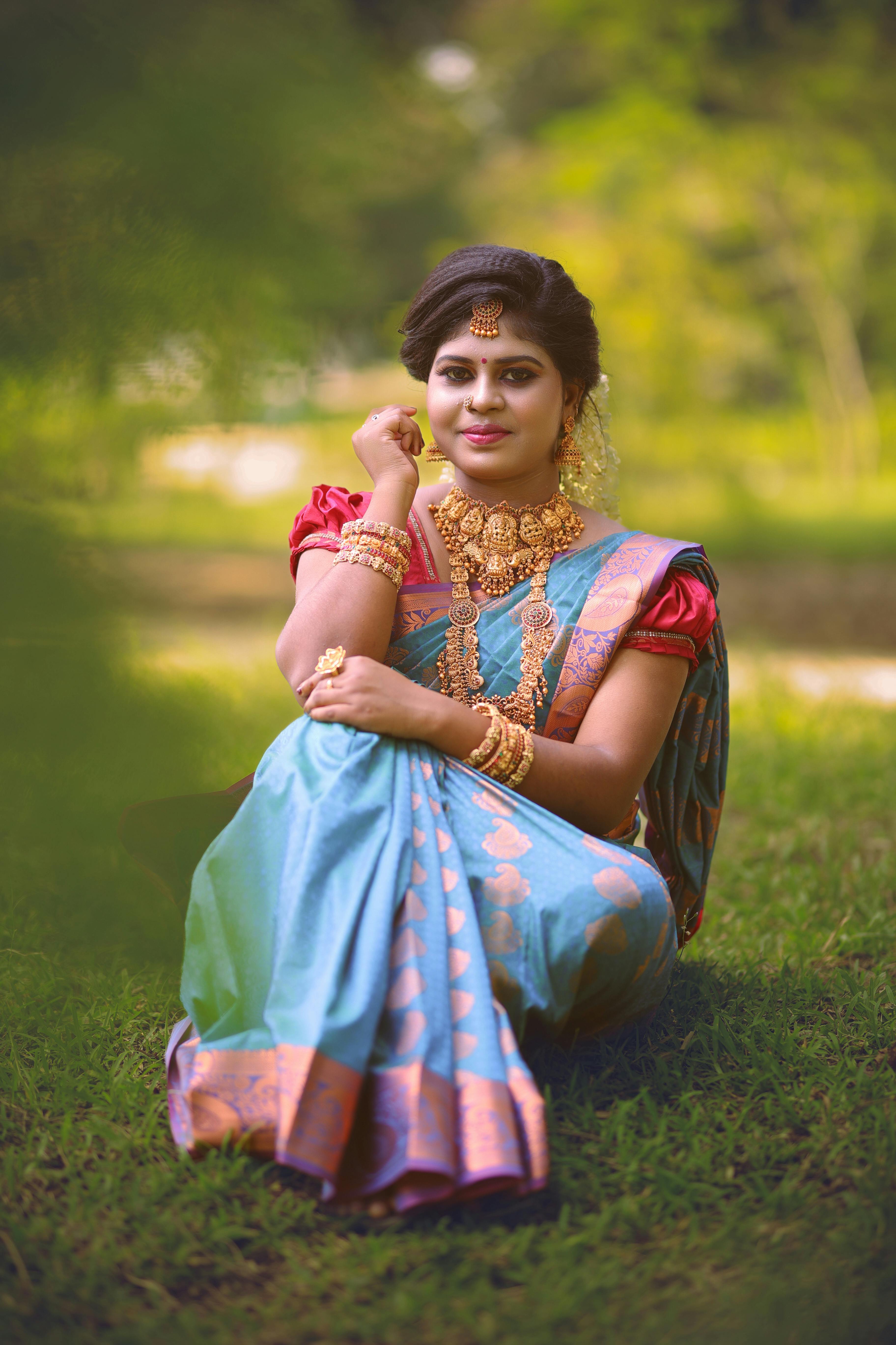 free photo of young woman in a colorful saree dress and jewelry sitting on the grass