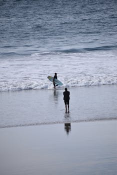 A surfer enters the ocean with a surfboard, ready to catch waves on a serene beach day.