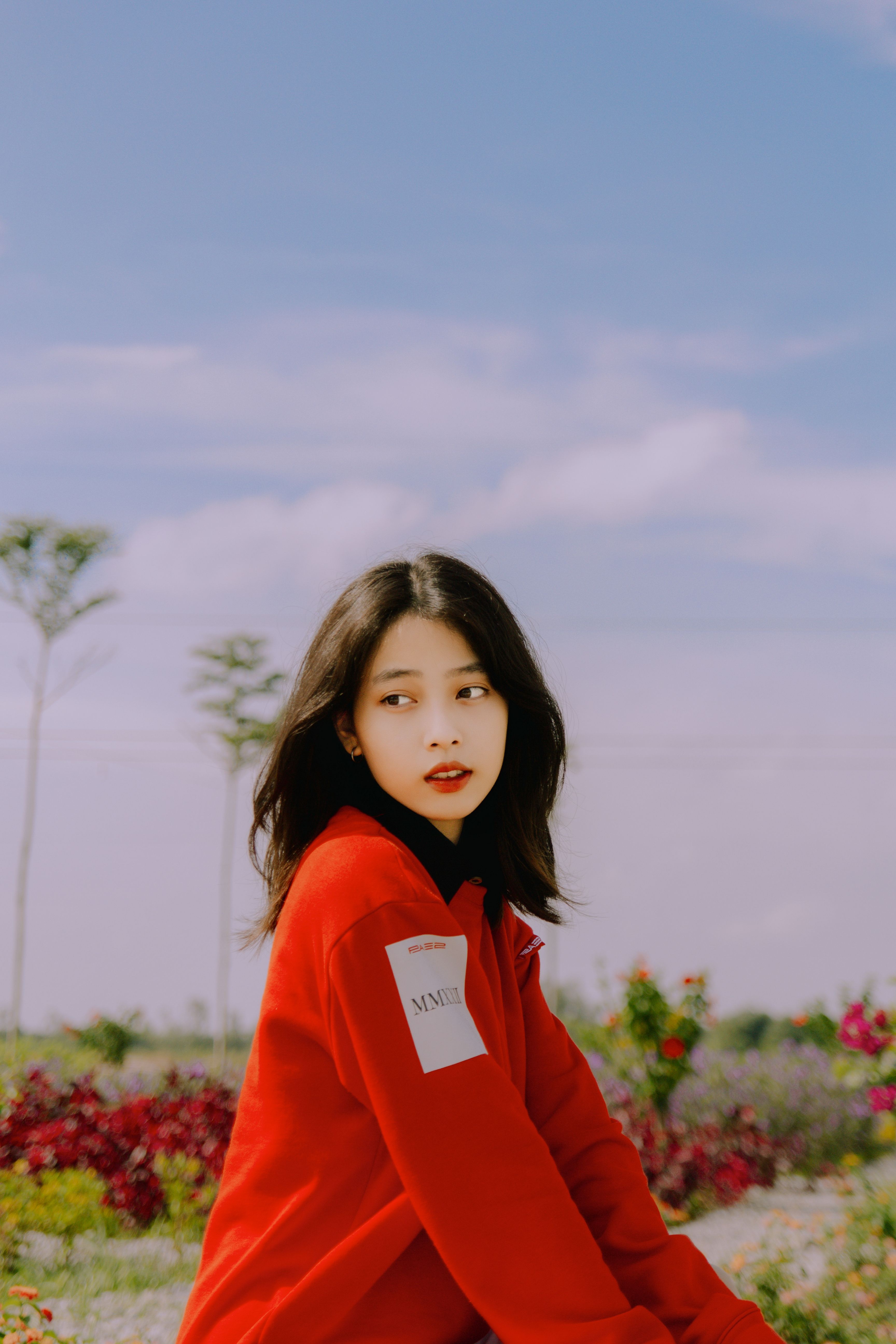 A captivating outdoor portrait of a young woman in a red sweater, sitting in a floral garden.