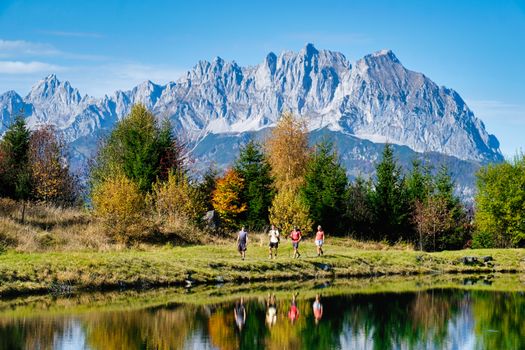 Group hiking by a serene alpine lake with stunning mountain backdrop in summer.