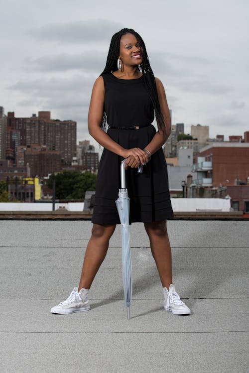 Young Woman in a Black Dress Standing on a Rooftop and Holding an Umbrella 