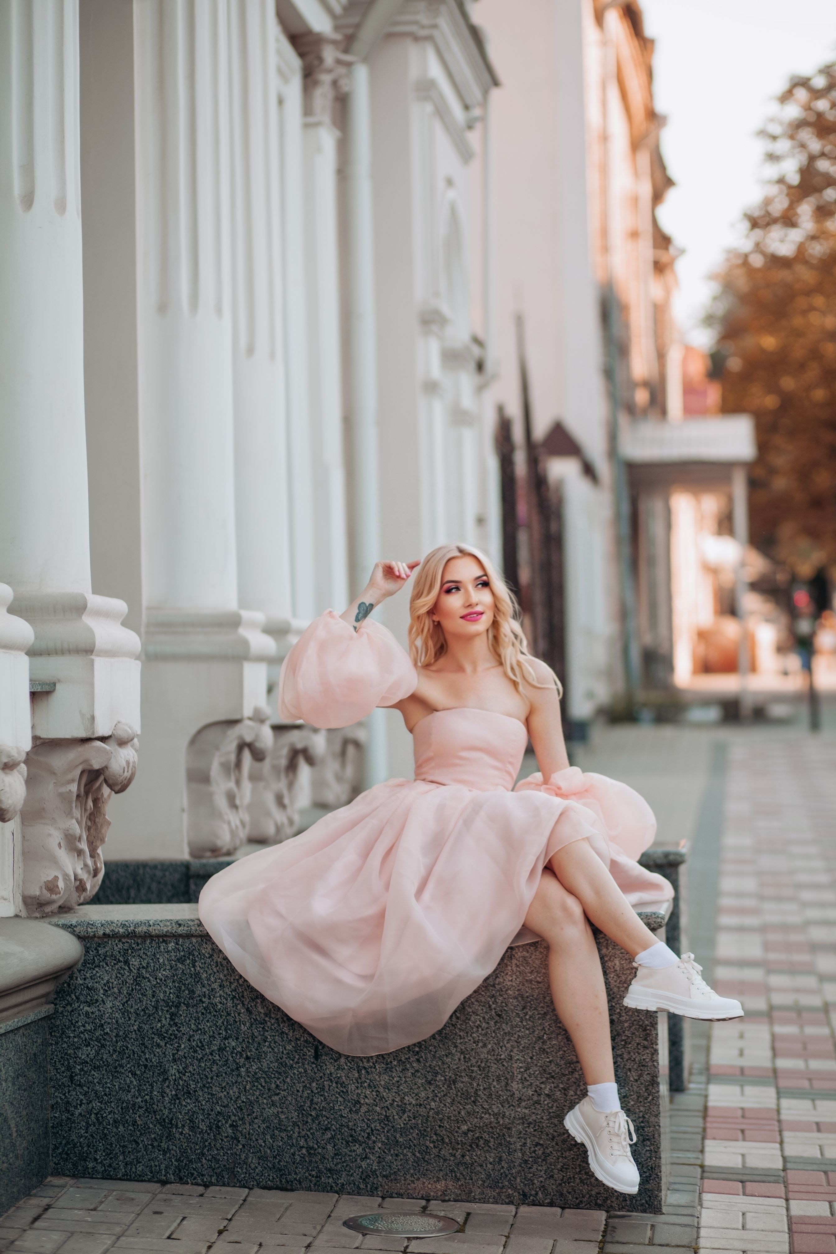 A blonde woman in a pink dress sitting on a bench · Free Stock Photo