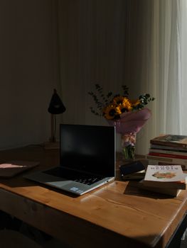 A warm home office setup featuring a laptop on a wooden desk with books and flowers, creating an inviting atmosphere.