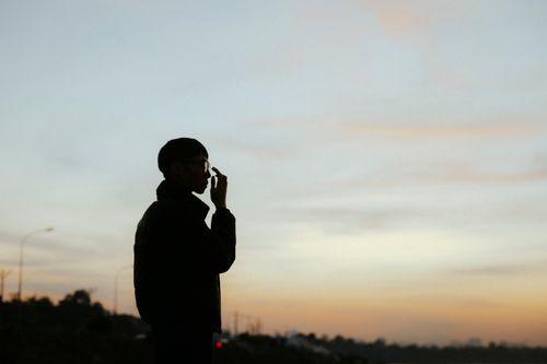 Free A man in silhouette adjusting his glasses at twilight, creating a dramatic outdoor scene. Stock Photo