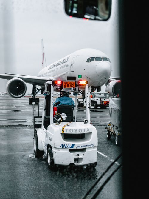 Free Airport ground crew operating a vehicle in front of a parked airliner on a rainy runway. Stock Photo