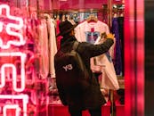 一名身着黑色外套、头戴帽子的男子正在一家灯火通明的精品店选购时尚服装