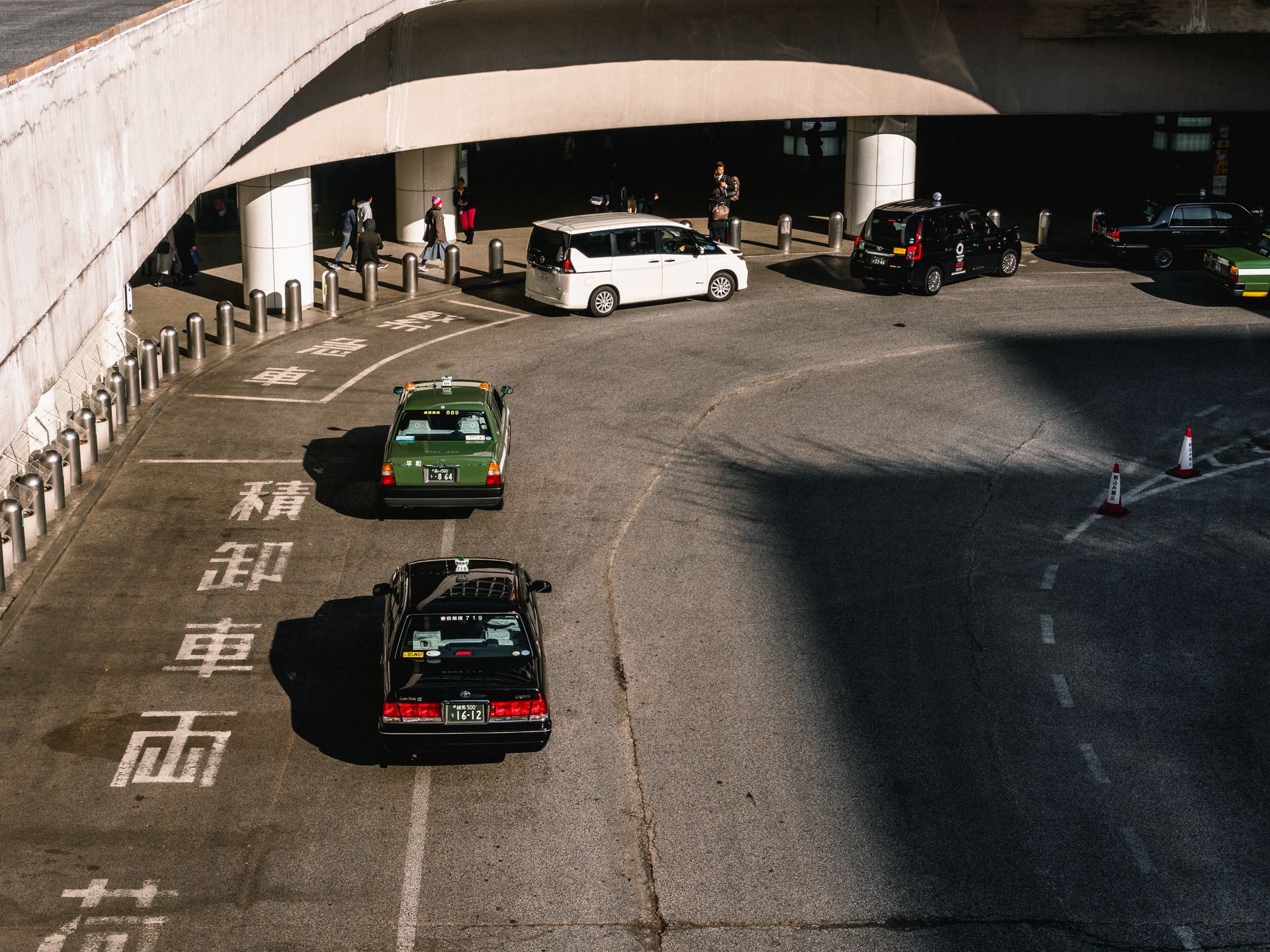 A bustling urban intersection with taxis and cars moving under an overpass in daylight.