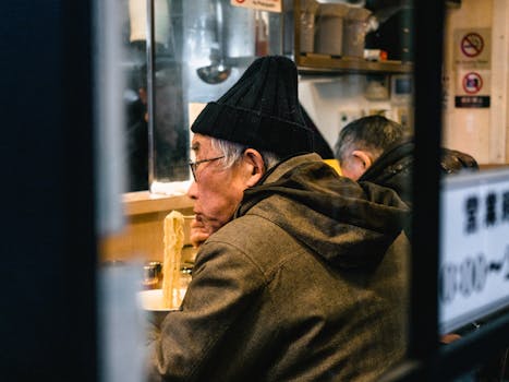 一位老人正在温暖舒适的餐厅里吃拉面，这是他的侧视图