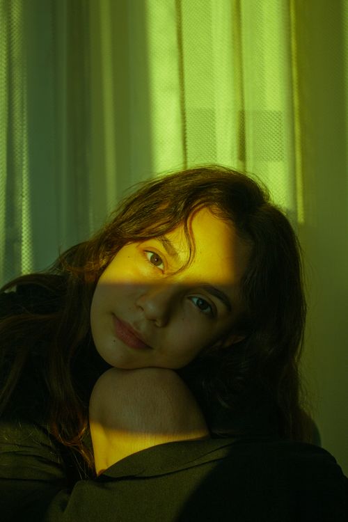 Free A serene portrait of a woman with long brown hair, bathed in warm sunlight indoors. Stock Photo