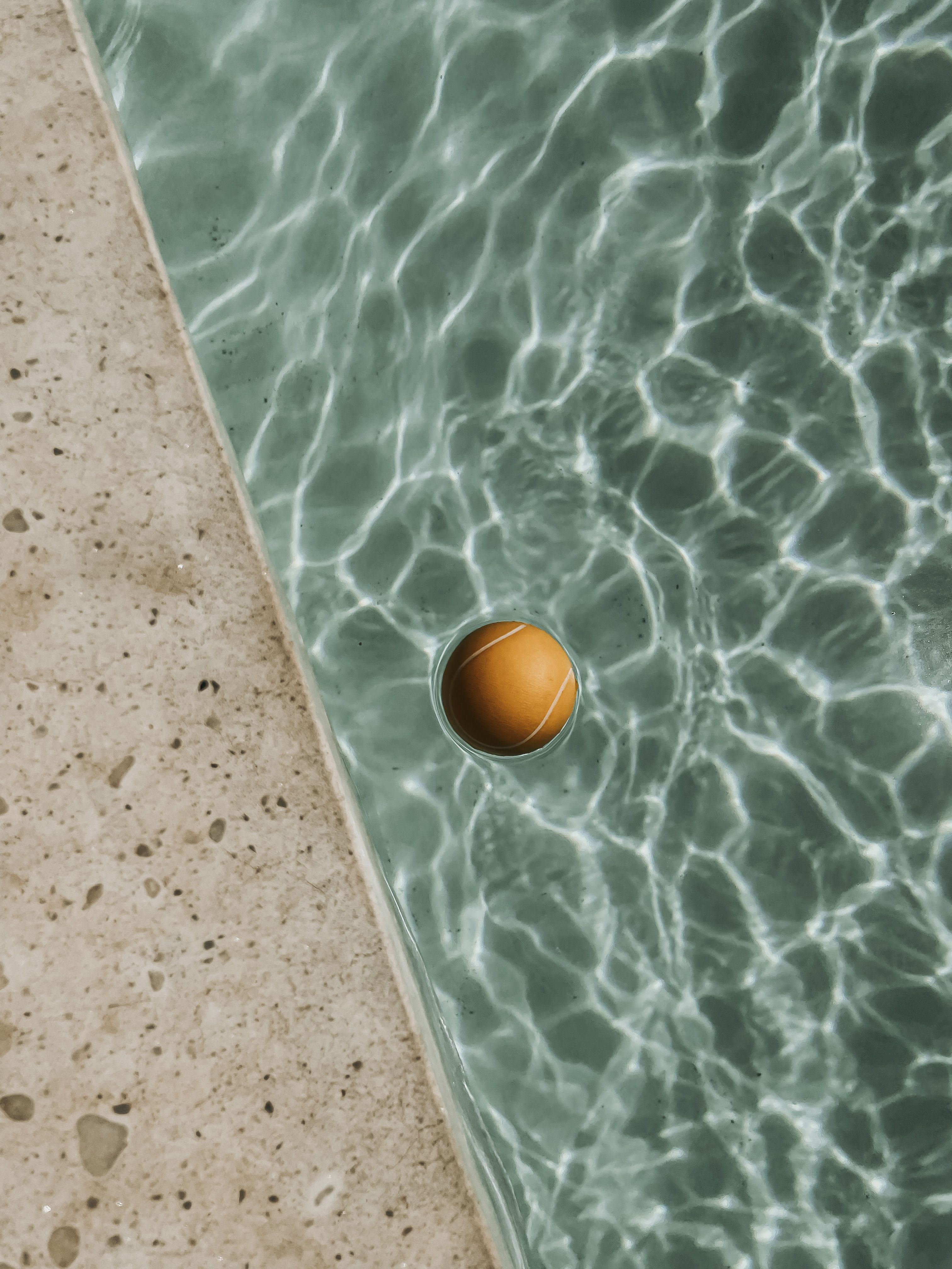 Orange ball in clear swimming pool creating reflections on a sunny day.