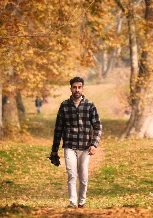 Free Man wearing checkered jacket walking through autumn leaves in Srinagar park. Stock Photo